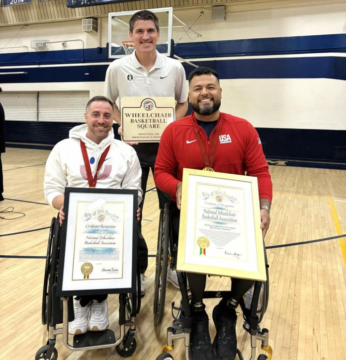 Two wheelchair basketball players smile while holding framed certificates, while a male official is holding a plaque that says wheelchair basketball square